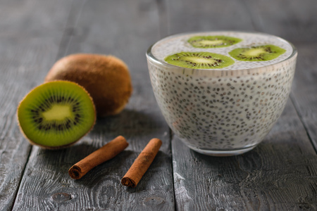 Two cinnamon sticks, kiwi fruit and a glass bowl of Chia seeds with milk on the village table. Diet food for weight loss and cleansing the body.の写真素材