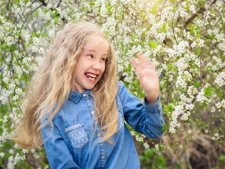 Beautiful girl with lush hair fun waves away hand in spring cherry garden. Portrait of laughing happy girl.の写真素材