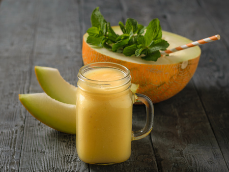 Half a melon with mint and a cocktail straw and a mug of smoothies on a wooden table. Diet drink for weight loss from the fruit.の写真素材