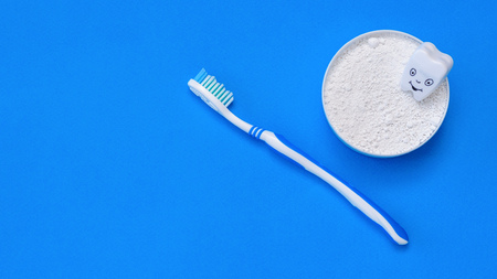 A cheerful tooth figure in a jar with tooth powder and a toothbrush on a blue background. Oral care products. The view from the top. Flat lay.の写真素材