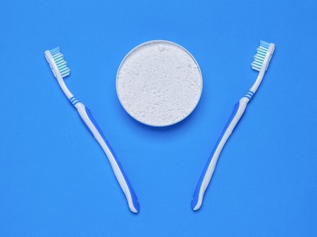 Two toothbrushes and a jar of tooth powder on the blue table. Oral care products. The view from the top. Flat lay.の写真素材