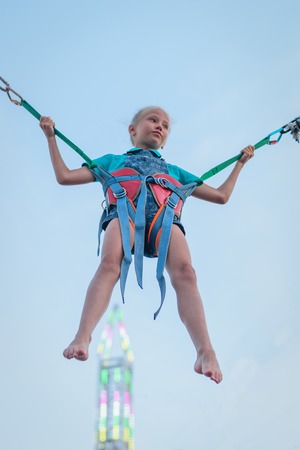 Girl hanging on rubber straps on the background of a glowing tower. A fascinating attraction in the amusement Park.の写真素材