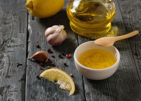 Olive oil with garlic and lemon in a white bowl on a dark table. Dressing for diet salad. Vegetarian food.の写真素材
