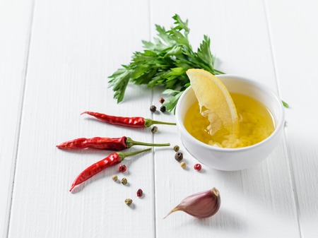 A slice of lemon in a Cup with olive oil, pepper and garlic on a white wooden table. Dressing for diet salad. Vegetarian food.の写真素材