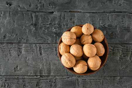A pile of walnuts in a clay bowl on a dark wooden table. Natural and dietary food. The view from the...