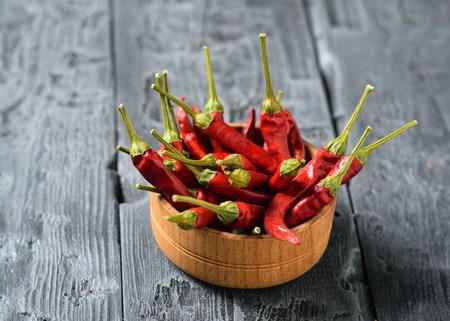 Chilli pods in a wooden bowl on a black wooden table. All-purpose seasoning. Vegetarian cuisine.の写真素材