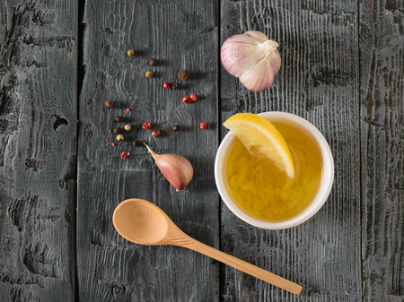 A head of garlic, olive oil, pepper and lemon on a black wooden table. Dressing for diet salad. Vegetarian food. The view from the top. Flat lay.の写真素材