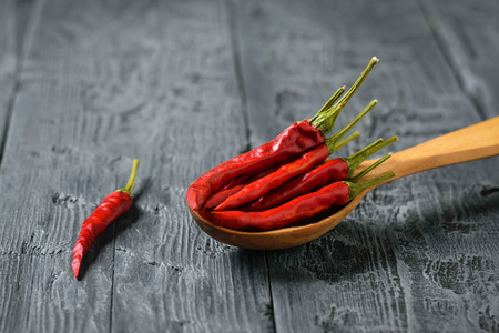 Chilli pods in a wooden spoon on a black wooden table. All-purpose seasoning. Vegetarian cuisine.