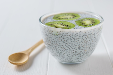 Wooden spoon, kiwi fruit and a glass bowl of Chia seeds with milk on the white table. Diet food for weight loss and cleansing the body.の写真素材