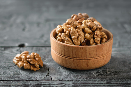 Pieces of peeled walnut in a wooden bowl on a dark wooden table. Natural and dietary food.の写真素材