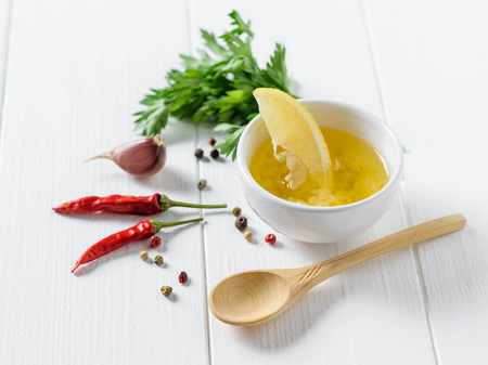 A slice of lemon in a Cup with olive oil, pepper and garlic on a white wooden table. Dressing for diet salad. Vegetarian food.の写真素材