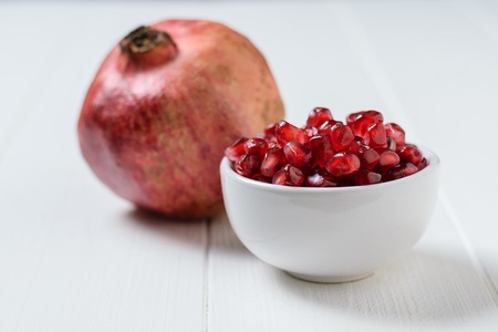 Seeds of ripe pomegranate in white Cup on white wooden table. Harvest ripe pomegranate . Vegetarian food. Raw food.の写真素材
