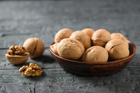 Split walnut with a clay bowl full of nuts on a dark rustic table. Natural and dietary food.の写真素材