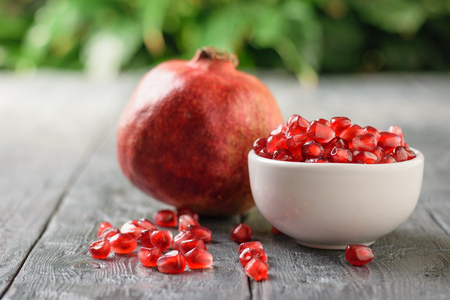 White Cup with pomegranate seeds and ripe pomegranate on black wooden table. Harvest ripe pomegranate . Vegetarian food. Raw food.の写真素材