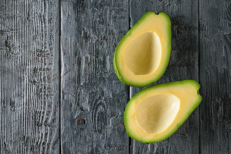 Two pitted avocado halves on a black wooden table. The view from the top. Flat lay.の写真素材
