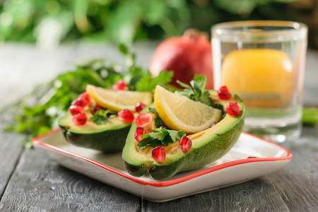 Avocado with pomegranate seeds, balsamic sauce, lemon and herbs on the black table. Vegetarian cuisine for weight loss. Healthy diet.の写真素材