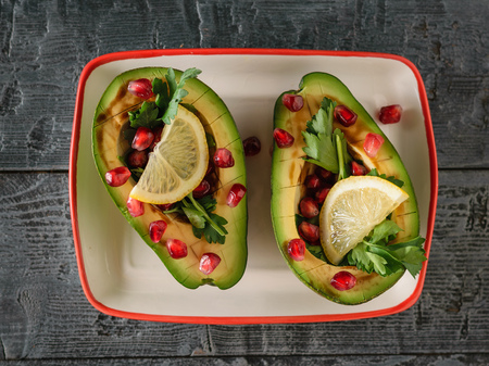 Avocado with pomegranate seeds, balsamic sauce, lemon and herbs on the black table. Vegetarian cuisine for weight loss. Healthy diet. The view from the top. Flat lay.の写真素材