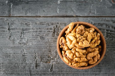 Pieces of peeled walnut in a wooden bowl on a dark wooden table. Natural and dietary food. The view from the top. Flat lay.の写真素材