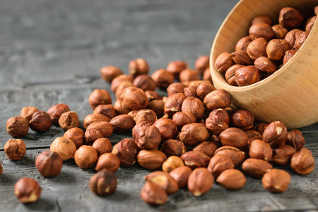 Hazelnut kernels are poured from a wooden bowl onto a dark wooden table. Natural diet vegetarian food.の写真素材