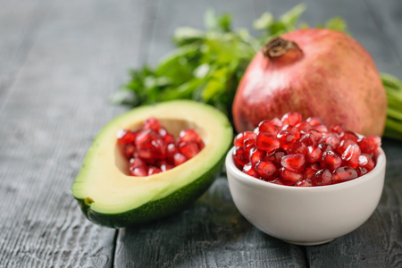 Half avocado with pomegranate seeds, bowl with pomegranate seeds, ripe pomegranate and parsley on a dark table. Ingredients of vegetarian cuisine.の写真素材