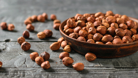 Scattered on a wooden table and in a clay bowl hazelnuts. Vegetarian cuisine. Autumn harvest.の写真素材