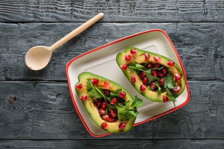 Avocado with pomegranate seeds, balsamic sauce, lemon and herbs on the black table. Vegetarian cuisine for weight loss. Healthy diet. The view from the top. Flat lay.の写真素材