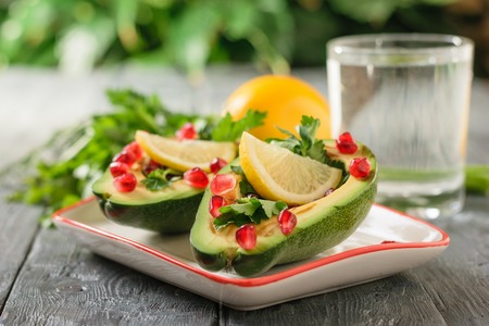 Avocado with pomegranate seeds, balsamic sauce, lemon and herbs on the black table. Vegetarian...