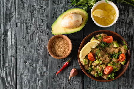 Clay bowl with amaranth seed salad with avocado, lemon, tomatoes and parsley on a dark wooden table. The view from the top. Flat lay.の写真素材