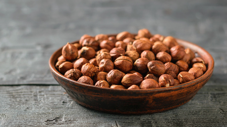 A clay bowl full of walnut kernels on a black rustic table. Vegetarian cuisine. Autumn harvest.の写真素材
