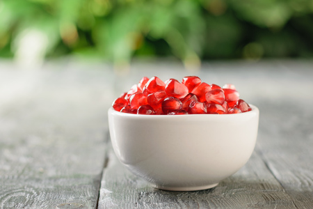 White Cup with pomegranate seeds and ripe pomegranate on black wooden table. Harvest ripe pomegranate . Vegetarian food. Raw food.の写真素材