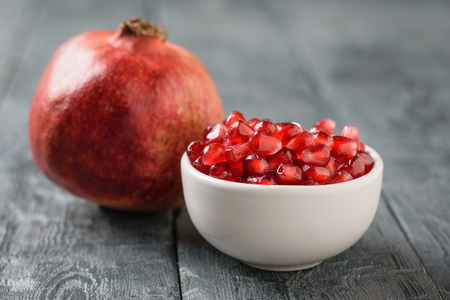 Ripe pomegranate and pomegranate seeds in a white bowl on a black wooden table. Harvest ripe pomegranate . Vegetarian food. Raw food.の写真素材
