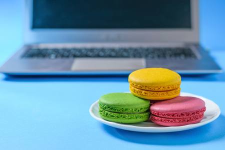 Colored macaroons in a white bowl on a blue background with the computer. Freshly made homemade macaroons.の写真素材
