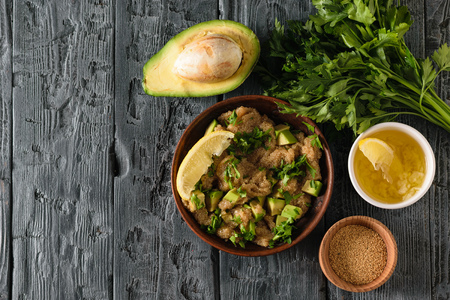 Clay bowl with amaranth seed salad with avocado, lemon, tomatoes and parsley on a dark wooden table. The view from the top. Flat lay.の写真素材