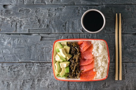 A plate of Hawaiian rice, avocado, salmon and kelp and soy sauce on a black wooden table. Mediterranean diet cuisine. The view from the top. Flat lay.の写真素材