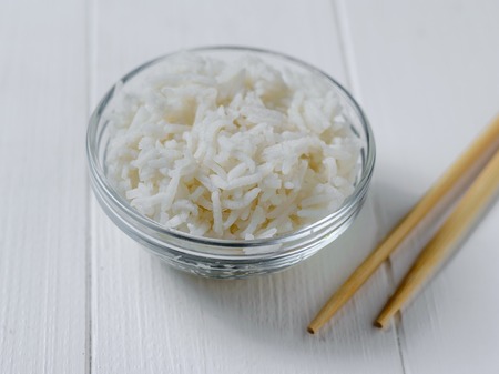 Wooden sticks next to a glass bowl of rice on a white wooden table. Natural diet food.の写真素材