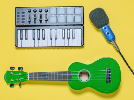 Green ukulele, blue microphone with wires and music mixer on yellow background. Equipment for recording music tracks. The view from the top. Flat lay.の写真素材