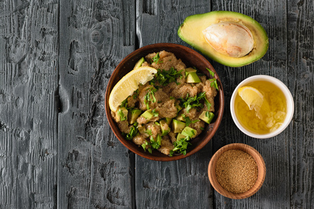 Clay bowl with amaranth seed salad with avocado, lemon, tomatoes and parsley on a dark wooden table. The view from the top. Flat lay.の写真素材