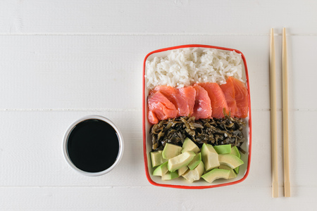 Bowl with long-grain rice, seaweed, avocado slices, salmon and wooden sticks on a white wooden table. Mediterranean diet cuisine. The view from the top. Flat lay.の写真素材