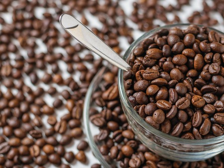 Glass bowl with coffee beans on white table background with scattered coffee beans. Grains for the preparation of the popular drink.の写真素材