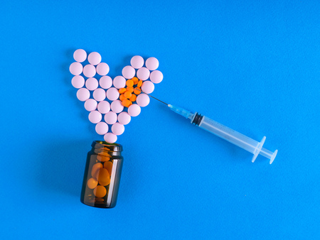 The needle of the syringe is aimed at the heart of the pills on a blue background. The view from the top. The concept of treatment and prevention of diseases. Flat lay.の写真素材