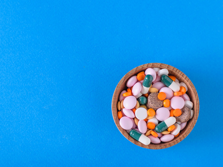 Many different colored tablets in a wooden bowl on a blue background. The view from the top. The...