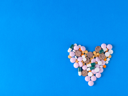 Heart made of colorful pills on blue background. The view from the top. The concept of treatment and...