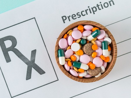 A sheet with a doctor's prescription and a wooden bowl with pills on a blue table. The view from the...
