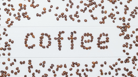 Beautiful coffee inscription made with roasted coffee beans on a white wooden table. The view from the top. Flat lay. Grains for the preparation of the popular drink.の写真素材