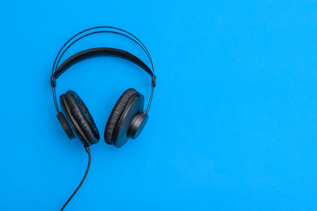 Black headphones with coiled cord on blue background. Accessory for listening to music and communication.の写真素材