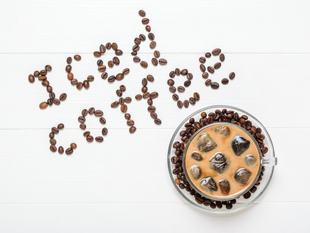 A Cup of coffee with floating icicles and an inscription of ice coffee on a white table. Refreshing and invigorating drink of coffee beans and milk. The view from the top. Flat lay.の写真素材