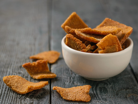 Pieces of dried bread in a white bowl on a black wooden table. Appetizer of dry bread with spices.