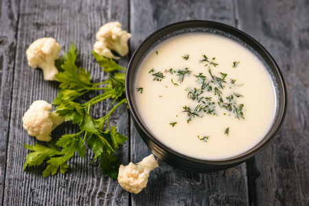 Scattered on the table inflorescences of cauliflower and a bowl of cream soup. Keto diet dish.の写真素材