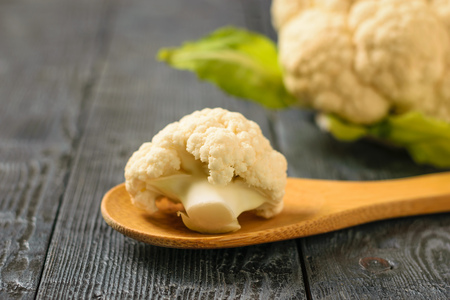 Inflorescence of cauliflower in a wooden spoon on a black wooden table. Healthy vegetarian diet.の写真素材