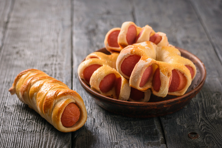 Fresh sausages in dough of various shapes on a black wooden table. Tasty meat snack made of dough and sausages.の写真素材